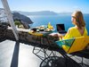 woman using a laptop and eating breakfast in front of a scenic view on vacation