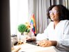 woman sitting at an office desk with a pride flag behind her